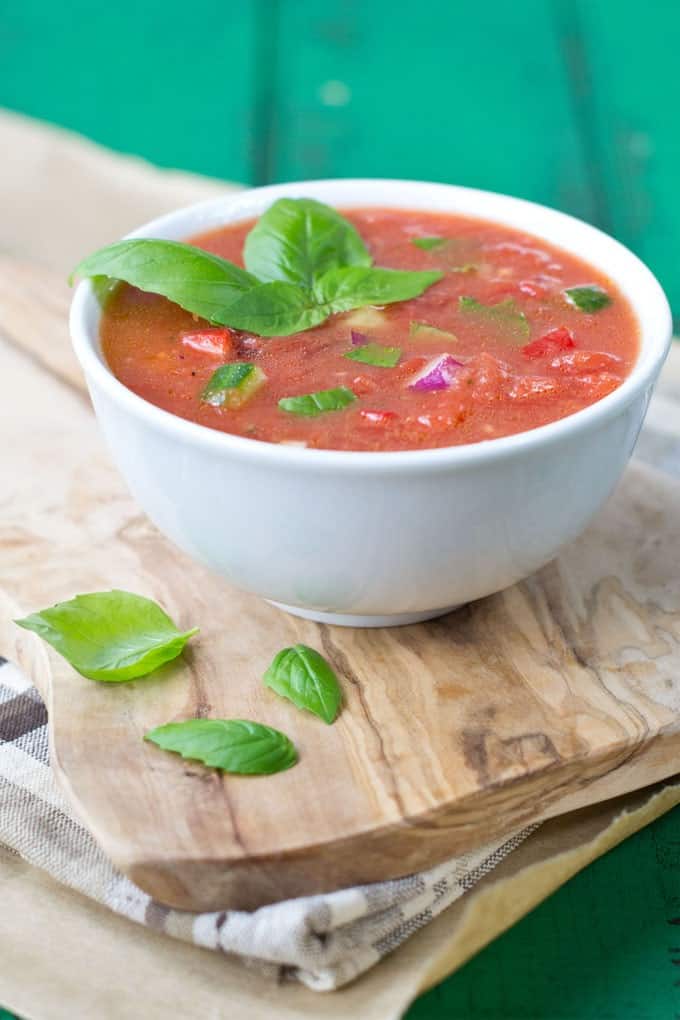 Gazpacho in a white bowl garnished with a sprig of basil.