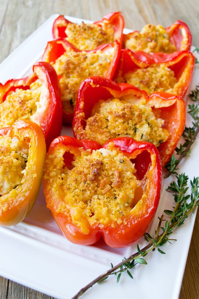Rectangular white platter filled with halved red peppers stuffed with chicken and topped with panko breadcrumbs that have been roasted to a golden brown; platter is garnished with thyme sprigs