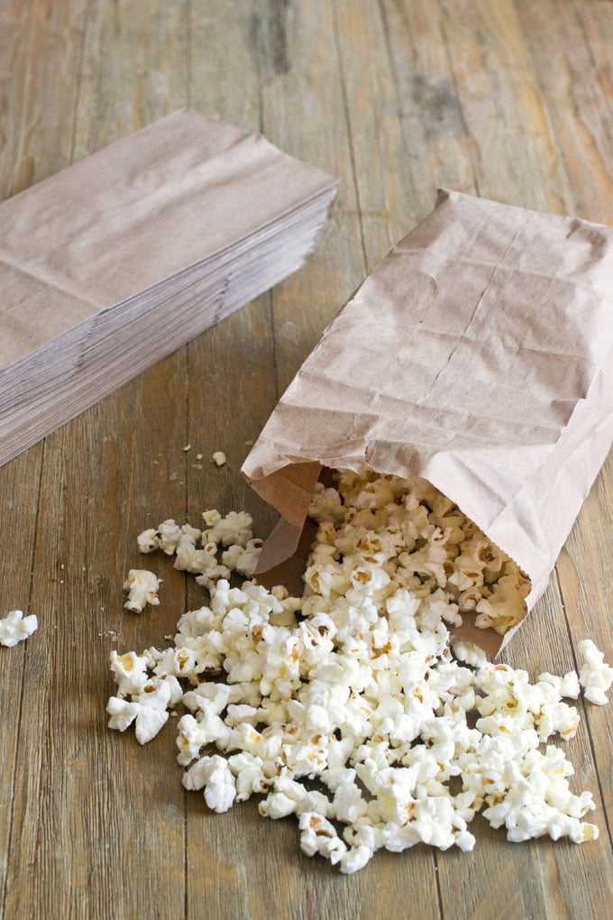 Brown lunch bag, tipped over on a wood table with popped popcorn spilling out