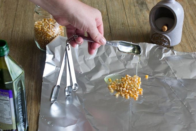 Get an 18" piece of heavy duty aluminium foil. Put 2 tablespoons of popcorn kernels in the middle of one half of the foil. Drizzle with 2 tablepsoons of oil (grape seed or vegetable oil).