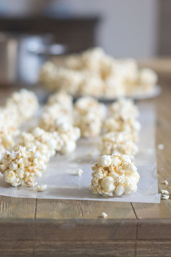 popcorn balls sitting on wax paper on a wood table.