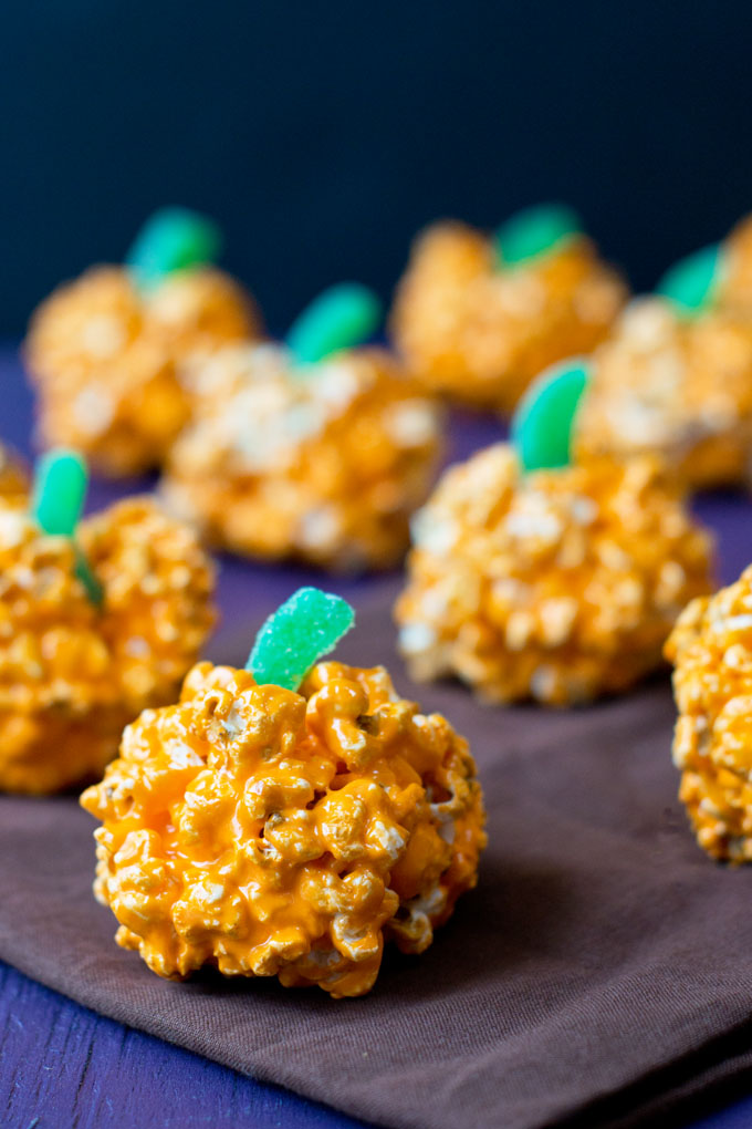 Orange Pumpkin Popcorn Balls with green stems made of candied gummy fruit strips; balls are sitting on a purple cloth napkin.