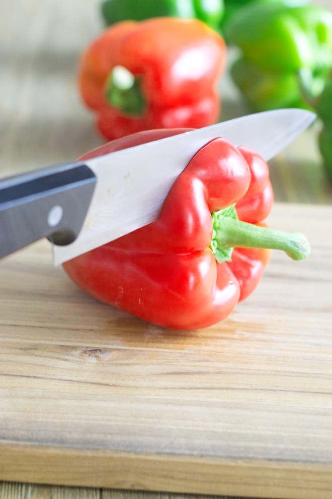 Chef's knife cutting the top off a red bell pepper.