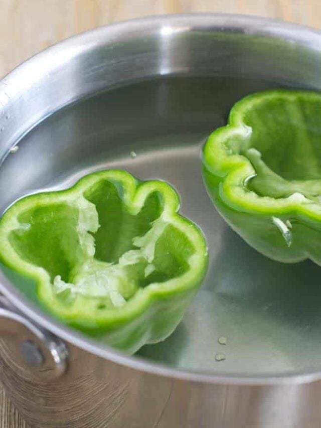 Green bell peppers are cut side up in a pot. Peppers are filled with water and the pot is full of water as well.