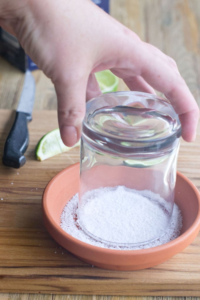 Tip the glass over into the salt. Now, I always do this like a cookie cutter, twisting it around. But I know other people say that leads to salt getting on the inside of the glass and falling into your drink. I like a bit of salt in my drink so I don't mind. If you do mind, what you do instead is to hold the glass at an angle such that only the outside planes of the glass touch the salt. 