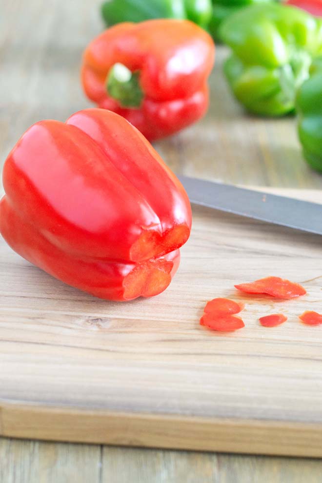 Whole red and green peppers sitting on a surface; the bottom points are cut off of one of the red peppers.