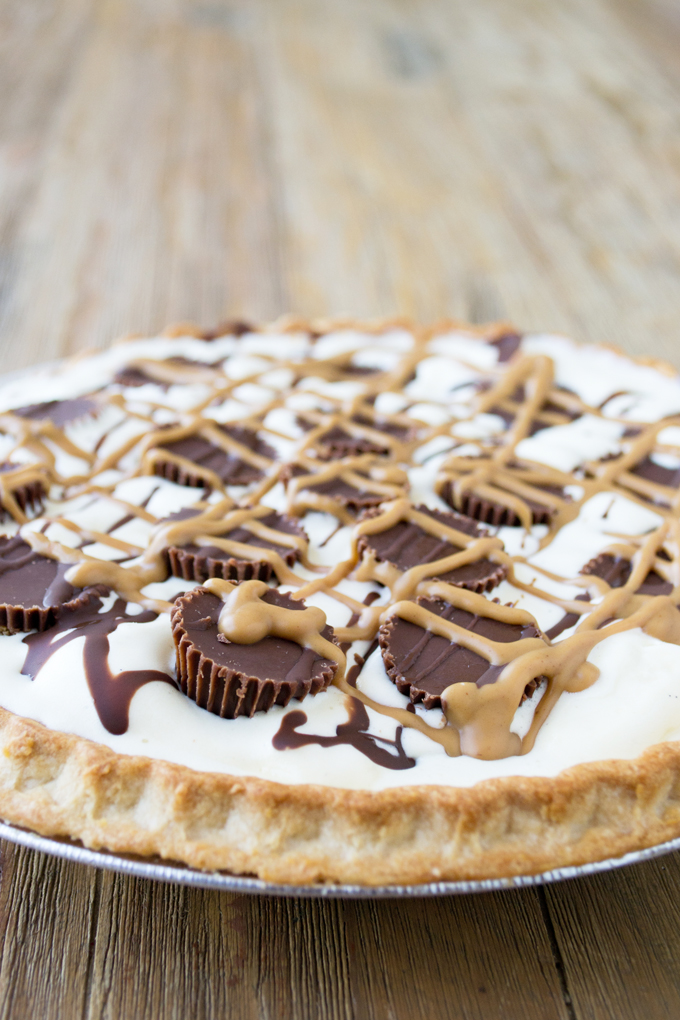 Picture of a Peanut Butter Cup Ice Cream Pie which is a pie shell filled with vanilla ice cream and topped with unwrapped peanut butter cups and drizzled with chocolate sauce and peanut butter.