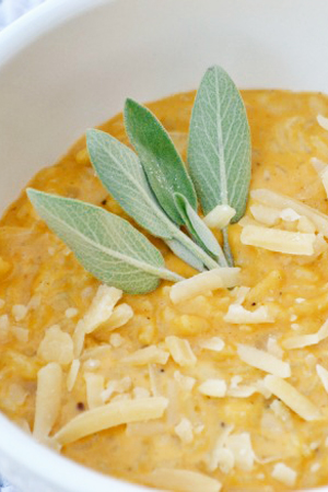 Savory Pumpkin Risotto with sage leaves on top in a white bowl.
