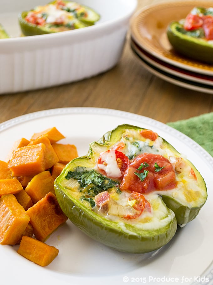 stuffed green bell pepper on a round white plate with some roasted sweet potatoes; in the background is a oval casserole dish with a stuffed pepper in it; next to the casserole dish is a stack of brown round plates with a stuffed pepper on it.