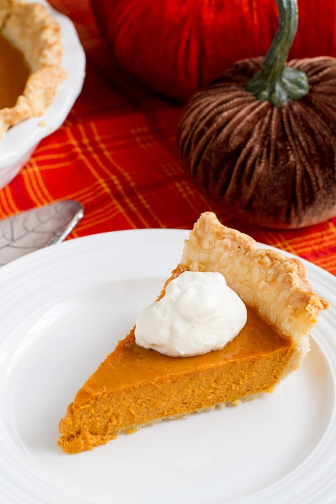 Slice of pumpkin pie with whipped cream on a white plate.