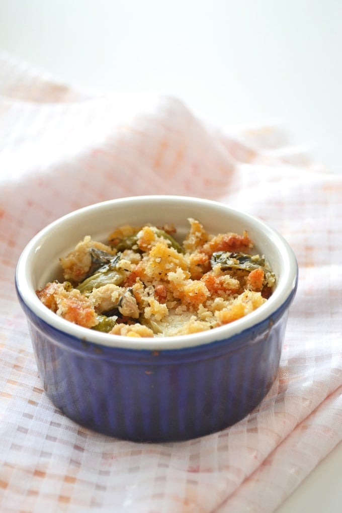 Blue ramekin on a peach colored checkered napkin filled with Brussels sprouts gratin topped with bread crumbs.