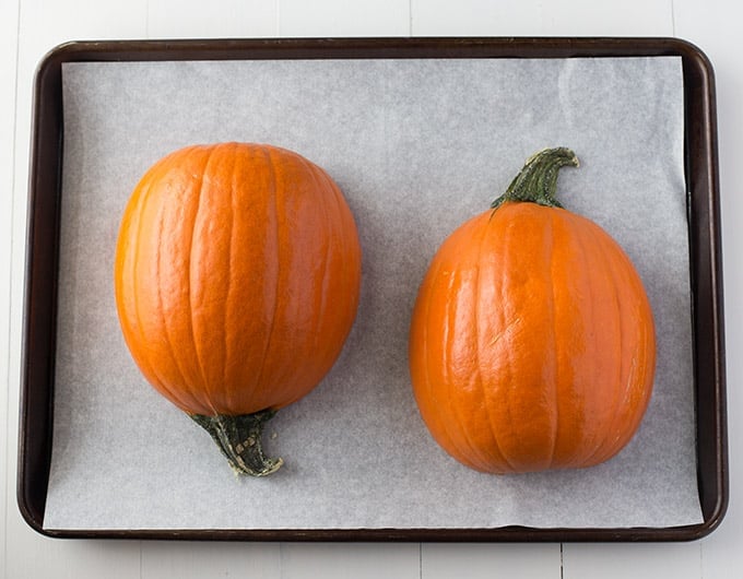 Pumpkin halves on parchment paper on a baking sheet.