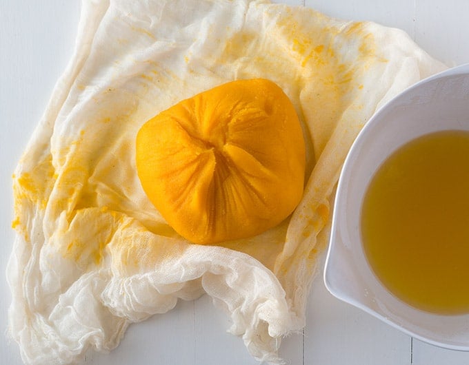 Thickened pumpkin puree in cheesecloth with strained liquid in white bowl.