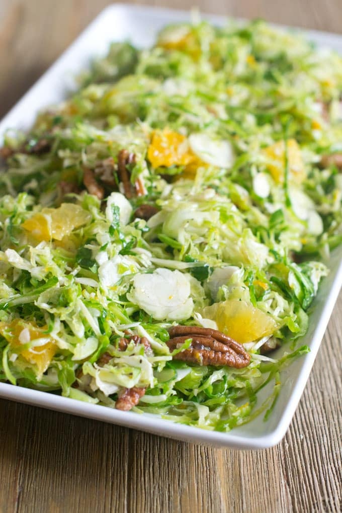 Close up of Brussels Sprouts Slaw with Orange and Pecans in a rectangular white dish on a brown table.