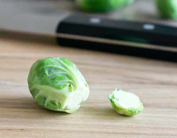 A single trimmed Brussels sprout on a cutting board. It has the stem end cut off and laying beside it. 