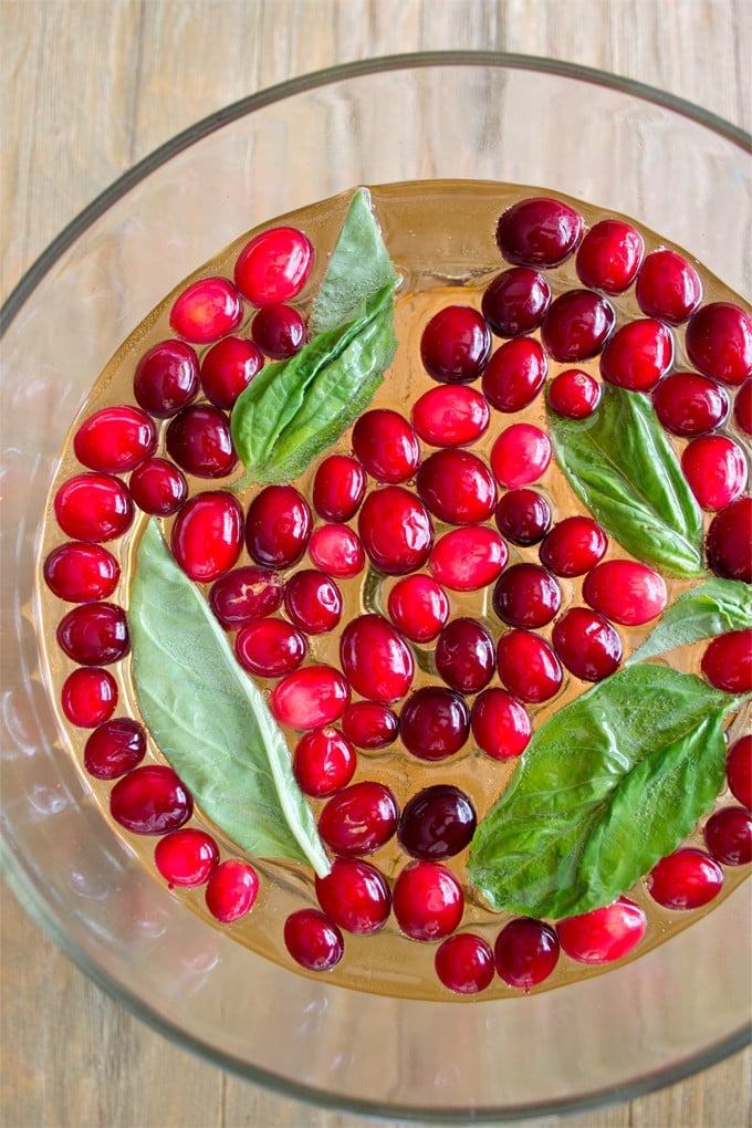 photo taken from directly above of a clear punch bowl filled with with whole cranberries floating in the punch with some whole basil leaves.