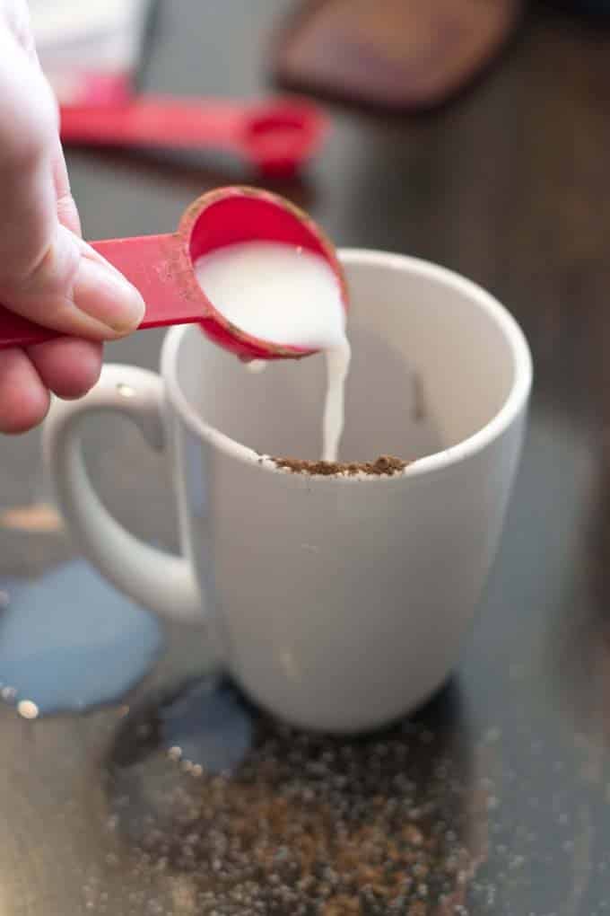 Measuring spoon of milk poured into white mug. 