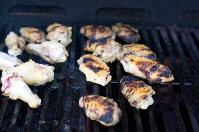 Grilling chicken wings, half flipped over showing grill marks.