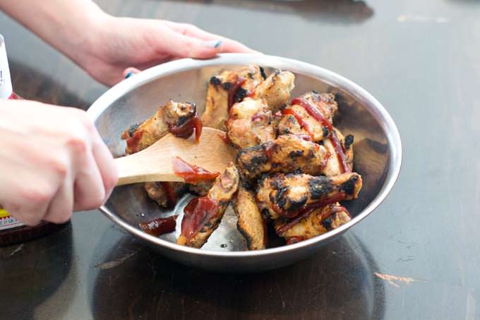 Mixing sauce and wings with wooden spoon.