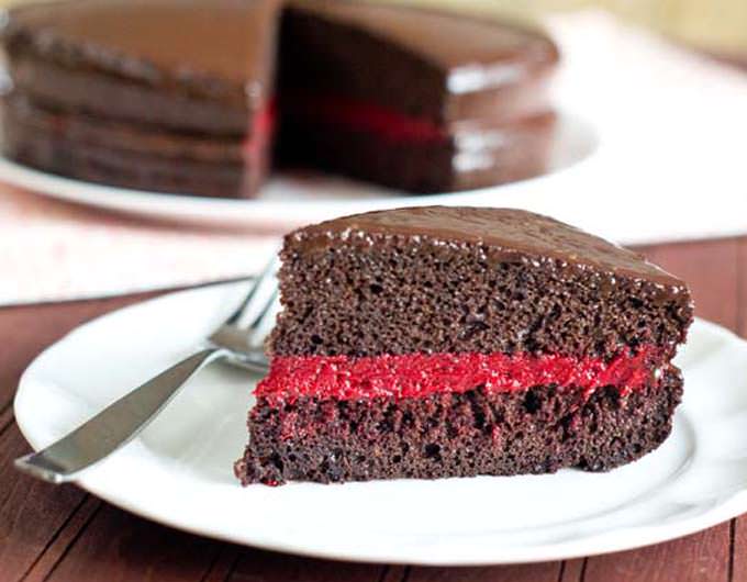Slice of chocolate cake with a red filling on a white plate.