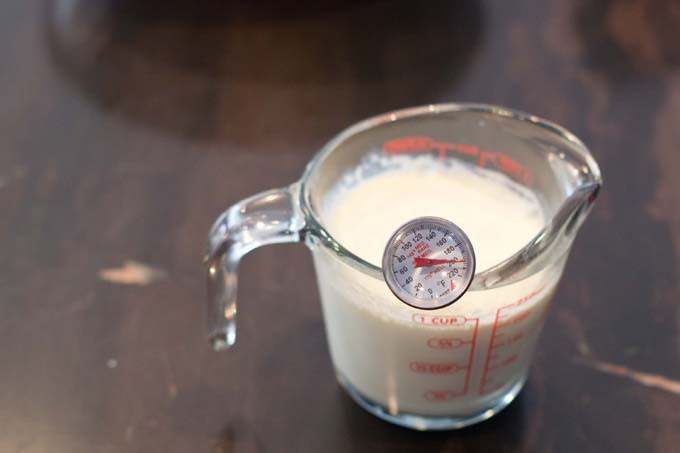 Heated cream in glass measuring cup with thermometer.