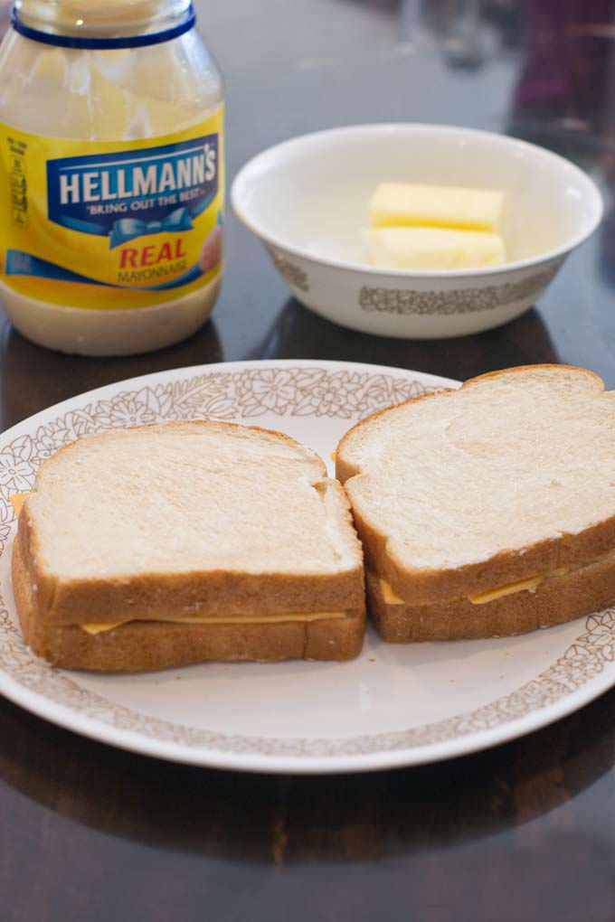 Two uncooked grilled cheese sandwiches on a plate with mayo and butter.