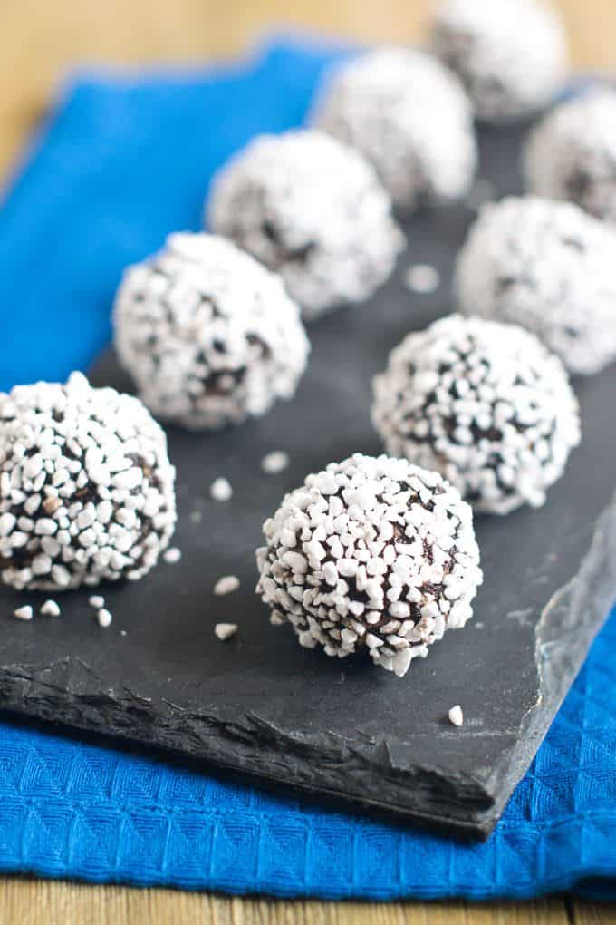 Swedish Chokladbullar - No-Bake Chocolate Balls - lined up in 2 rows on a black slate serving dish sitting on a blue dish towel.