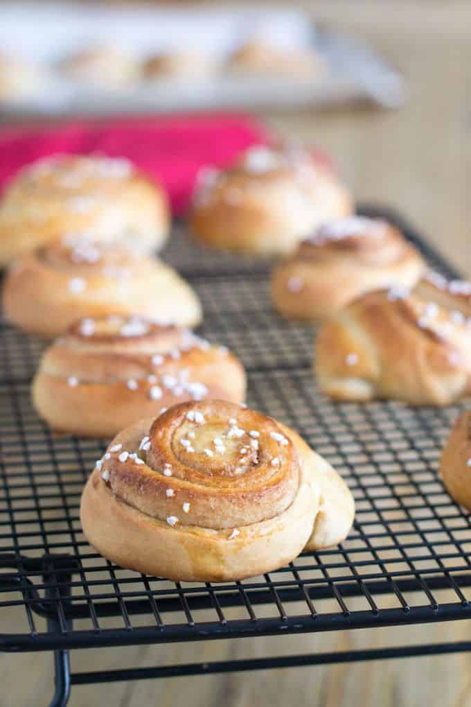 8 Swedish Cinnamon Bun (Kanelbullar) - sitting on a black wire rack with a pink dish cloth in the background.