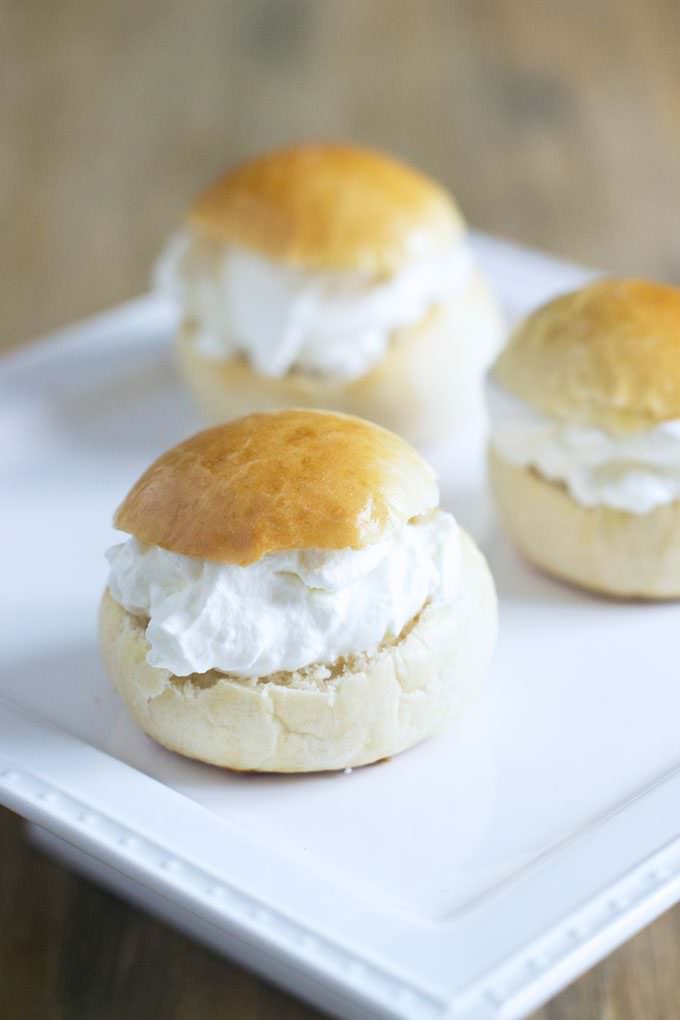 Square white plate with 3 Swedish Semlor on it. Swedish Smelor look similar to small cream puffs.