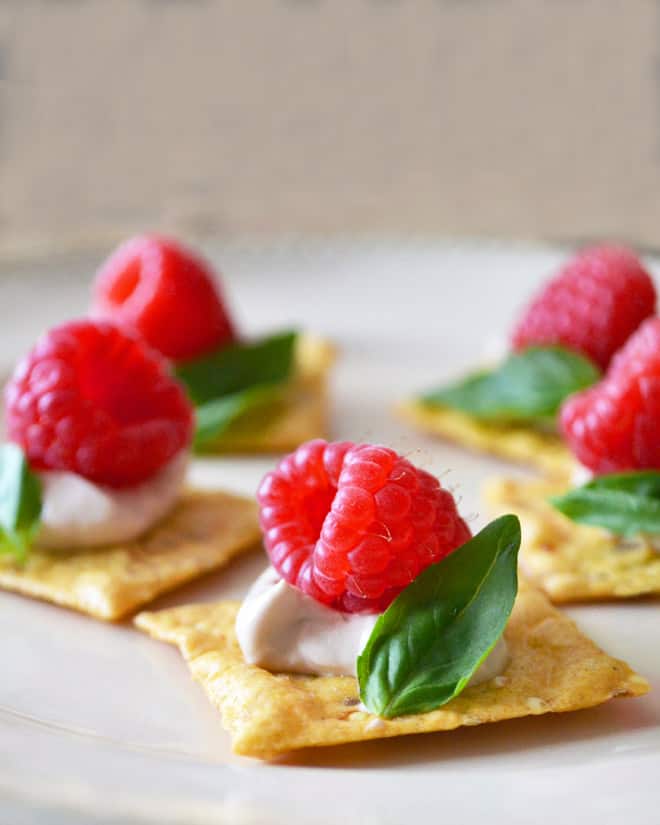 Crackers with a dollop of cream, fresh raspberry, and basil leaf.