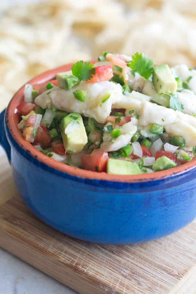 Blue ceramic bowl filled with ceviche with avocados, chopped tomatoes, diced jalapenos, onions and cilantro.