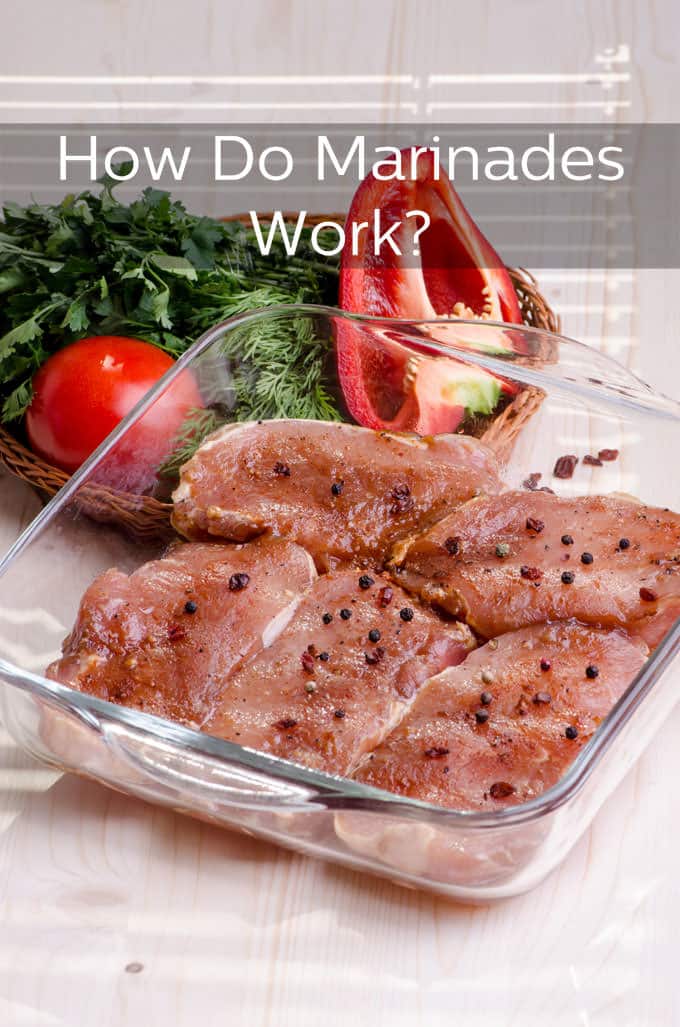 Raw pork chops in a square glass baking dish seasoned with spices and peppercorns. In a basket behind the dish is a basket filled with red pepper, a tomato, fresh dills and fresh flat leaf parsley.