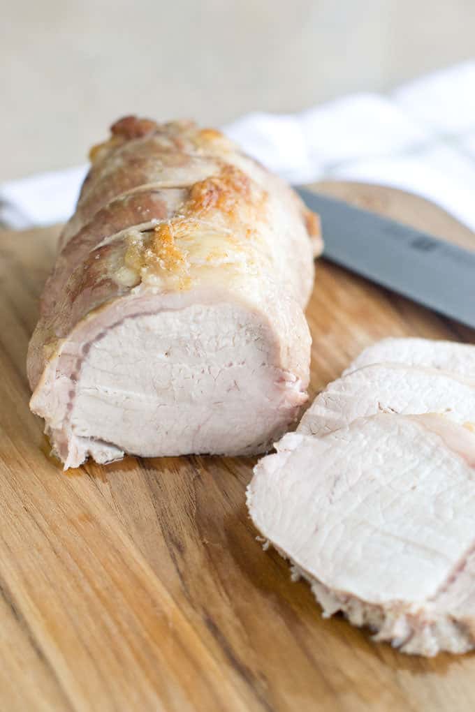 Roasted pork loin on a cutting board that has several slices cut and a knife laying next to the roast pork.