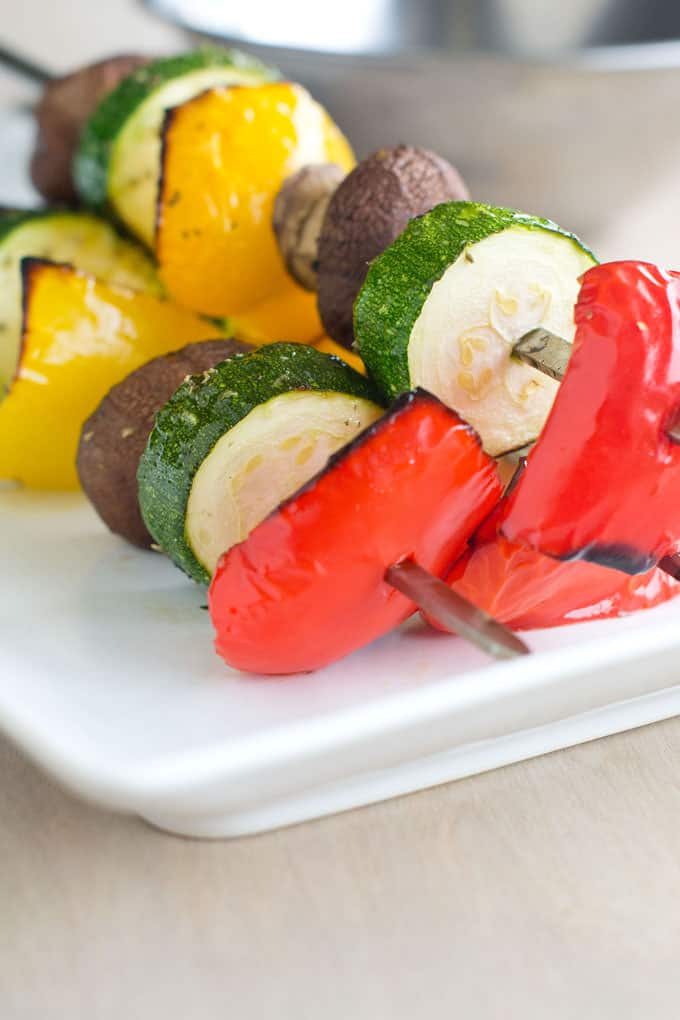 Broiled vegetable skewers with red pepper, zucchini, mushrooms and yellow peppers on an rectangular platter.