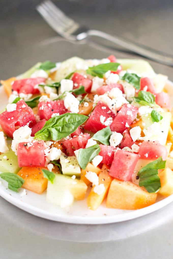 Plate of watermelon, honeydew, and cantaloupe chunks with feta and fresh basil.