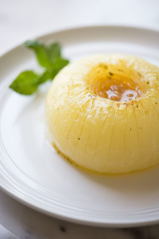 lightly golden baked onion on white plate with sprig of basil