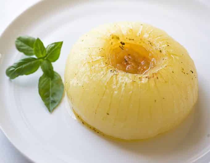 Whole Baked Onion on a white plate with fresh basil leaves.