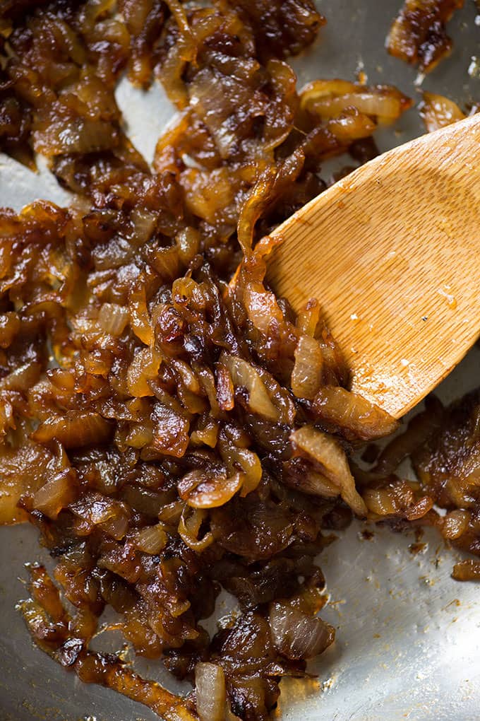 Stovetop caramelized onions in pan with wooden spoon.