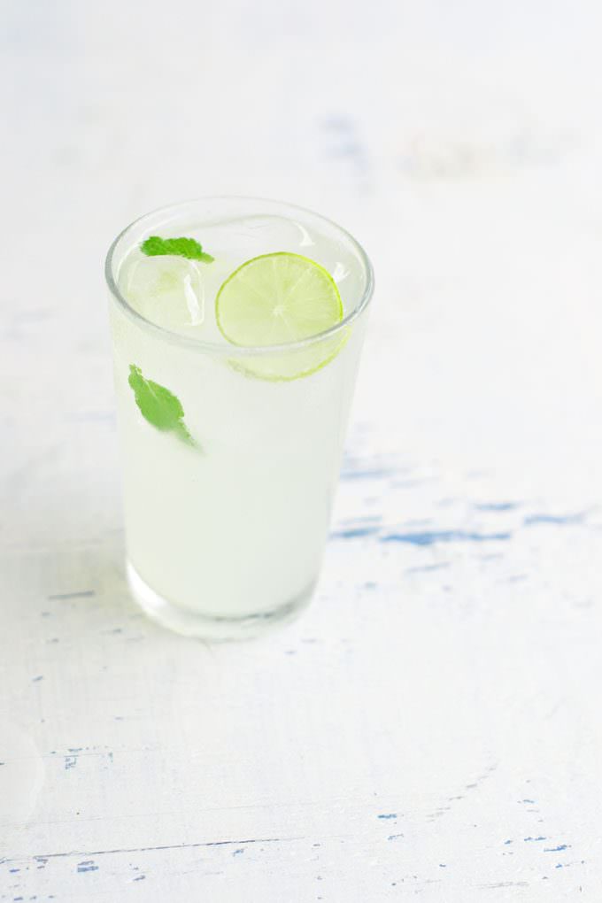 Tall glass of Key Lime Lemonade with a slice of lime and a few mint leaves floating in it.