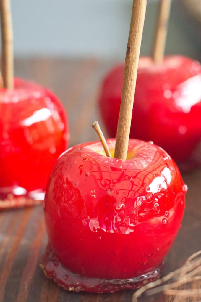 Three red apples coated in candy with rustic sticks coming out of the tops.