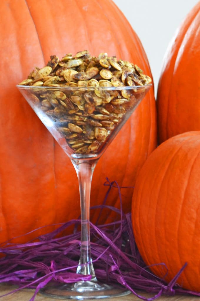 Pesto Parmesan pumpkin seeds in a martini glass in front of pumpkins.
