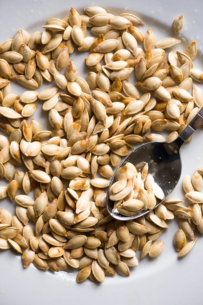 Salted pumpkin seeds on a white plate with a spoon.