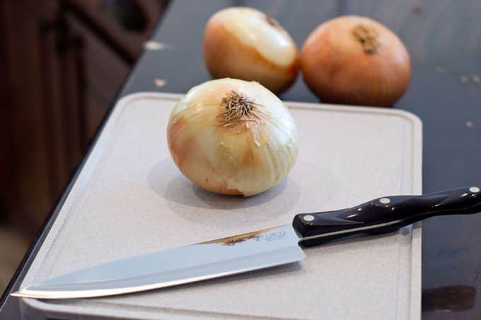 Whole onion on cutting board with chef's knife.