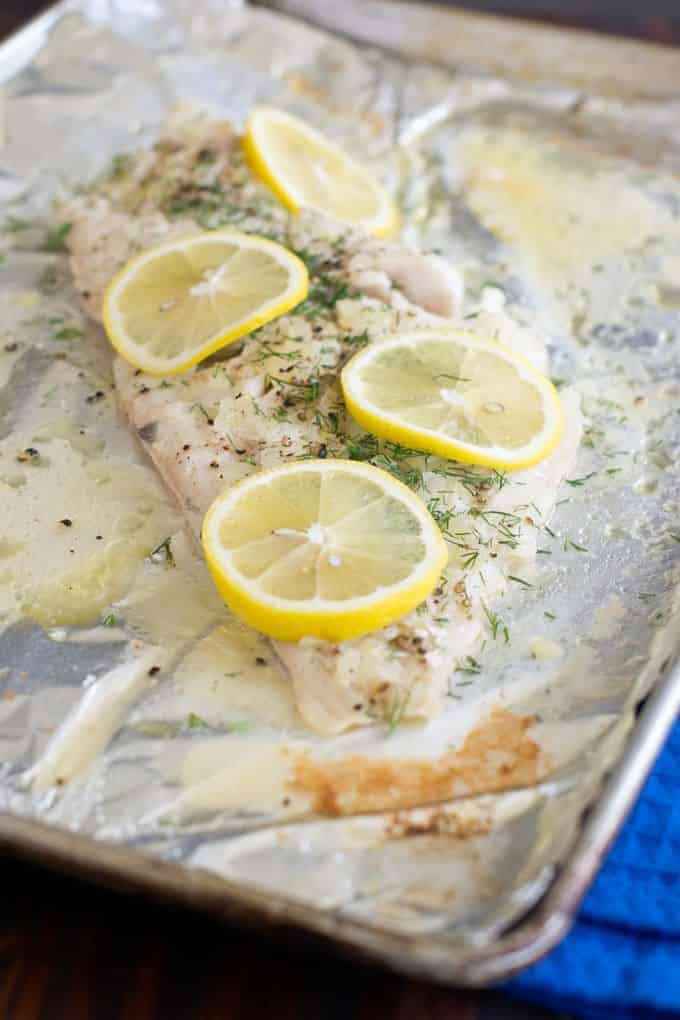 Baked Haddock on a foil covered sheet pan, topped with fresh dill and lemon slices.