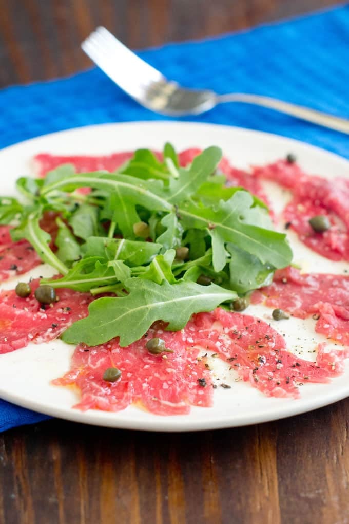 Beef carpaccio on a white plate with capers and arugula.