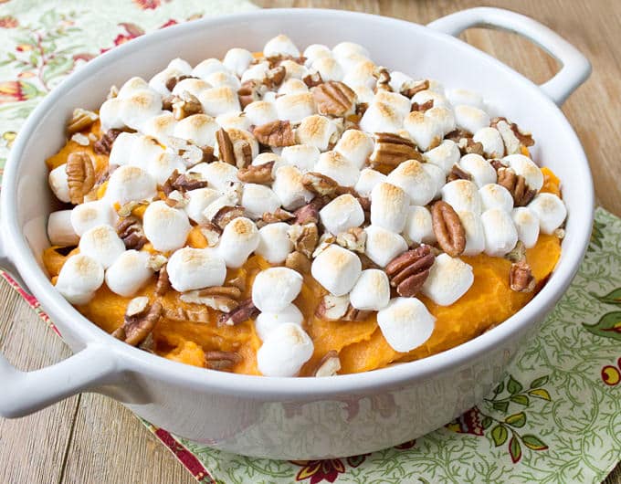 white casserole dish with mashed sweet potatoes topped with toasted marshmallows and chopped pecans; cream colored cloth with red orange flowers under dish