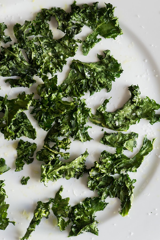 Crispy kale chips on a white plate sprinkled with flaky sea salt.