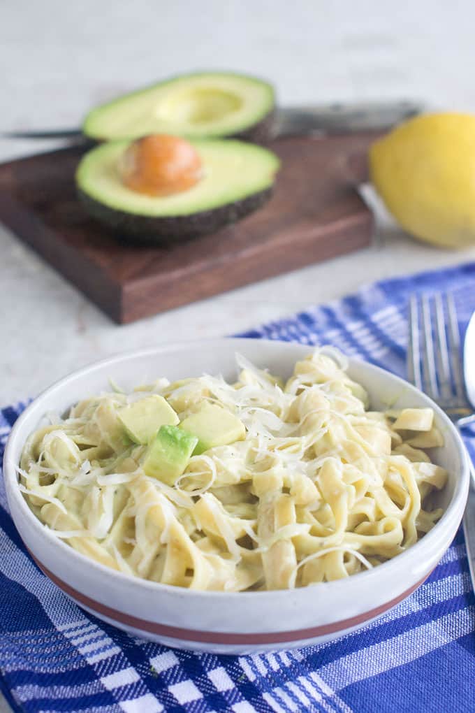 Alfredo with diced avocado and shredded cheese in a bowl, avocado and lemon in background.