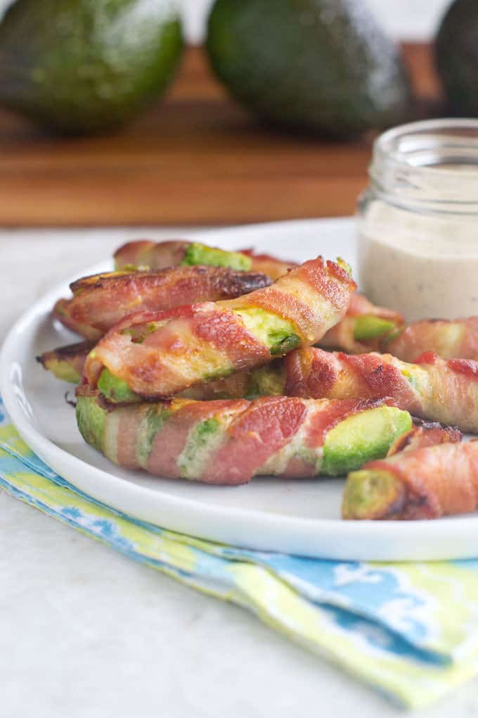 White plate filled with Bacon Wrapped Avocado Fries with a jar of ranch dressing in the background.