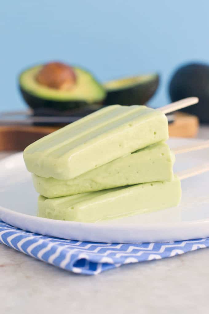 stack of avocado popsicles with raw avocados in the background.